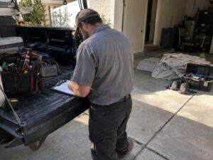 Technician wrapping paperwork on a work truck tailgate by Aegis Heating and Air